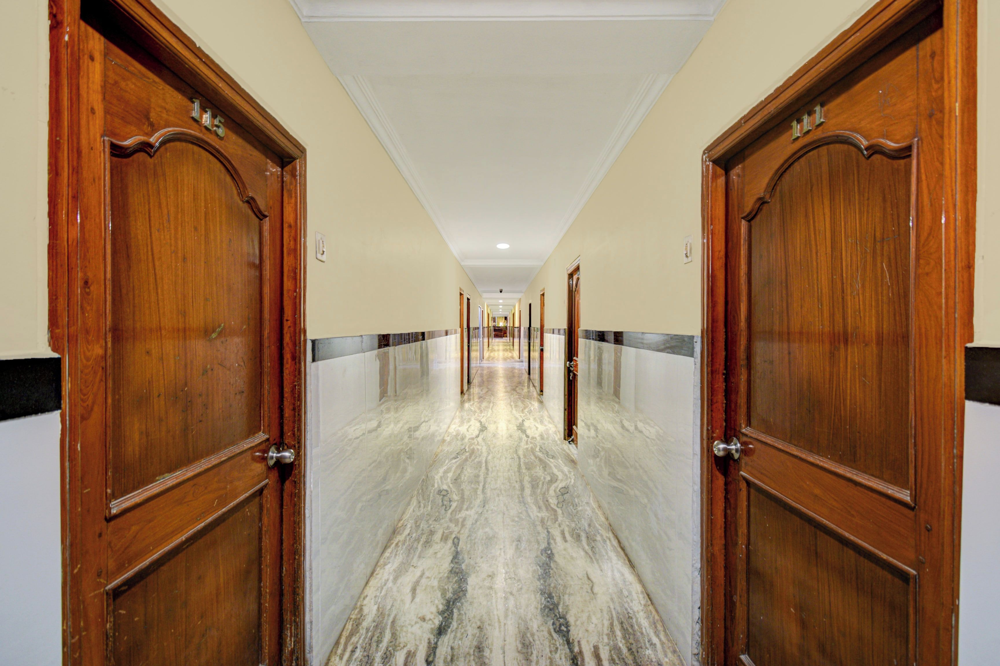 Un pasillo con puertas de madera, paredes blancas y suelo de mármol.