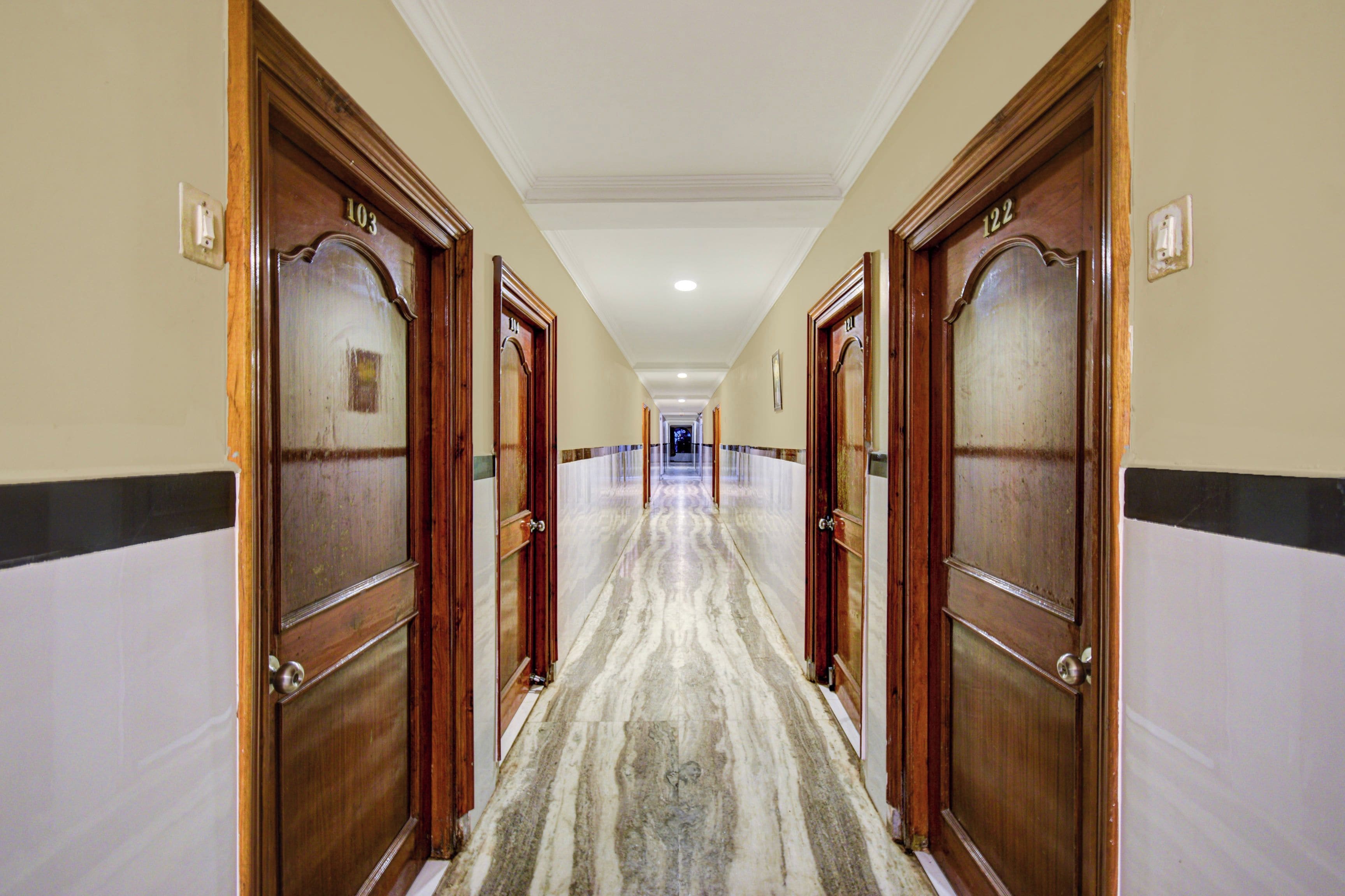 A hotel hallway with wooden doors numbered 103 and 122, marble flooring, and a white ceiling.