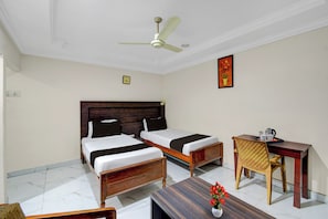 A hotel room with two single beds, a wooden desk, a chair, a ceiling fan, and a clock on the wall.