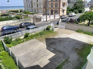 Rua residencial com carros estacionados, portão fechado e edifícios ao fundo.