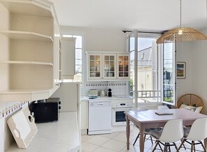 A compact kitchen with white cabinets, a dining table with chairs, and a large window with a view of the outside. - New Listing (Cabourg)