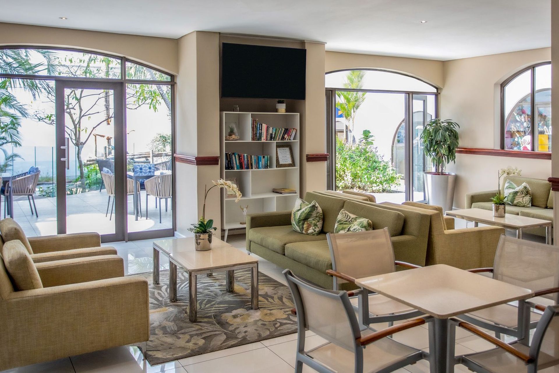 A modern living room with a sofa, chairs, a coffee table, and a bookshelf. There is a large window providing a view of the outdoors.