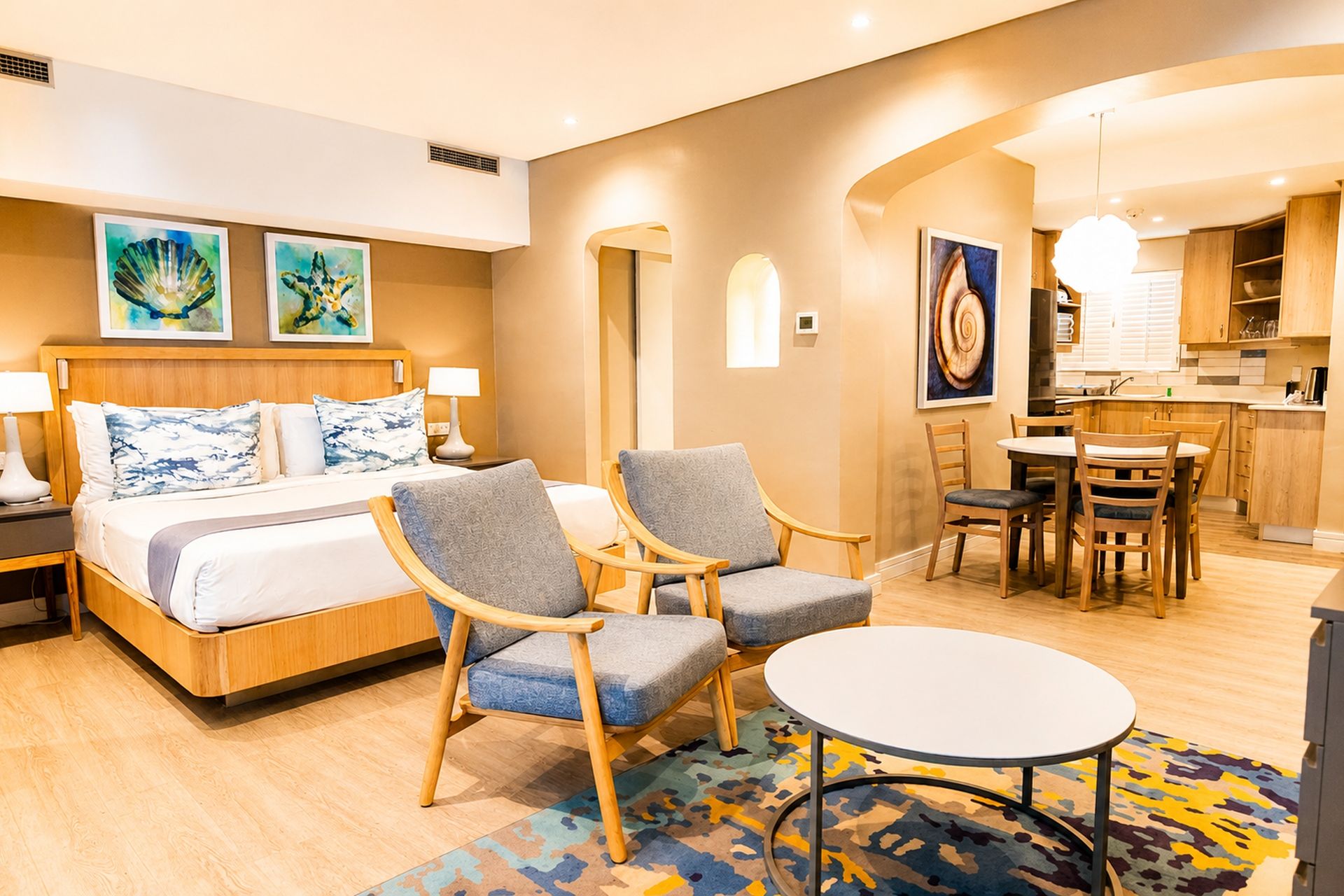 Una habitación de hotel con cama, dos sillones, una mesita y una kitchenette.