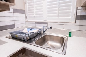 A kitchen with a stainless steel sink, a window with blinds, and a countertop with a dish rack. - Champagne Sports Resort (Central Drakensburg)