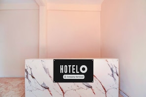 Bancada de recepção de hotel com tampos de mármore e uma placa com a inscrição 'HOTEL O Company Serviced'.