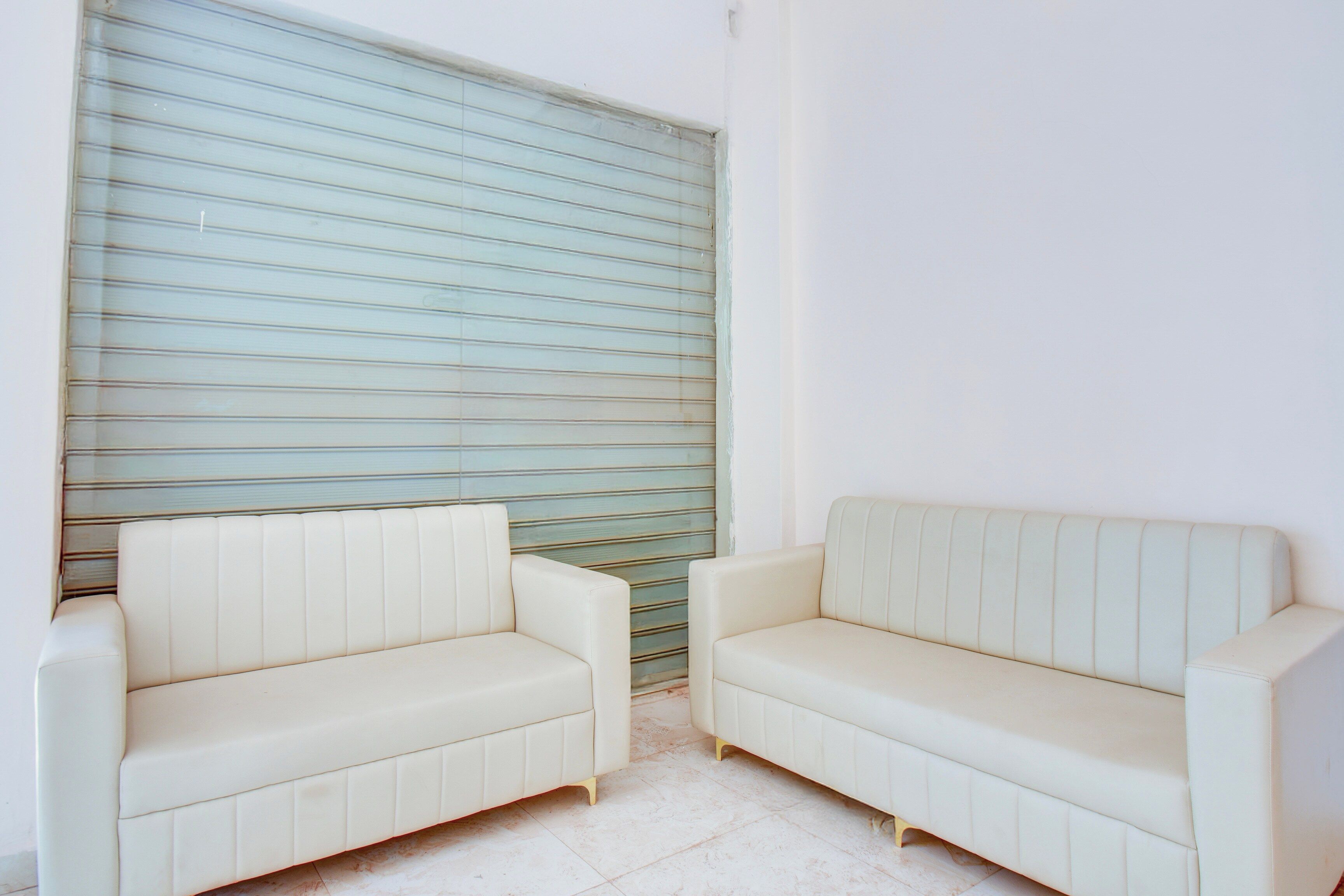 A room with two white sofas against a wall with horizontal lines, a tiled floor, and a plain white wall.