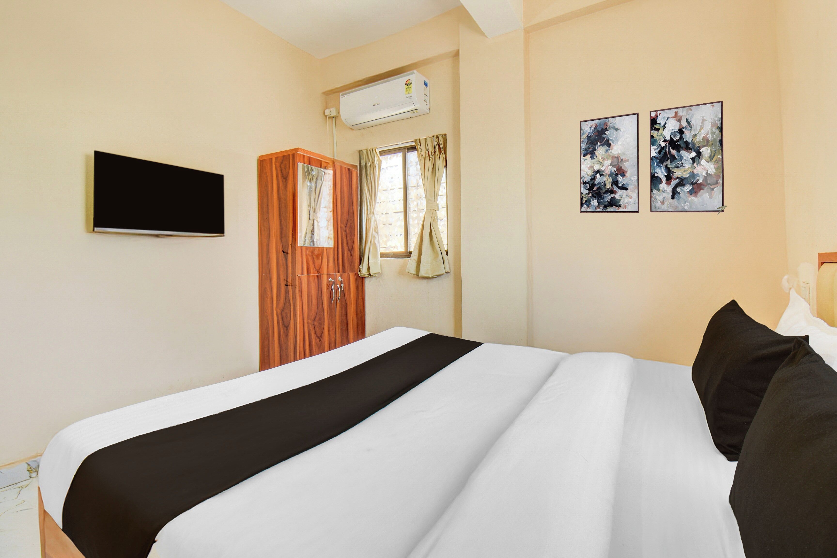 A hotel room with a bed, a wardrobe, a flat-screen TV, and two abstract paintings on the wall.