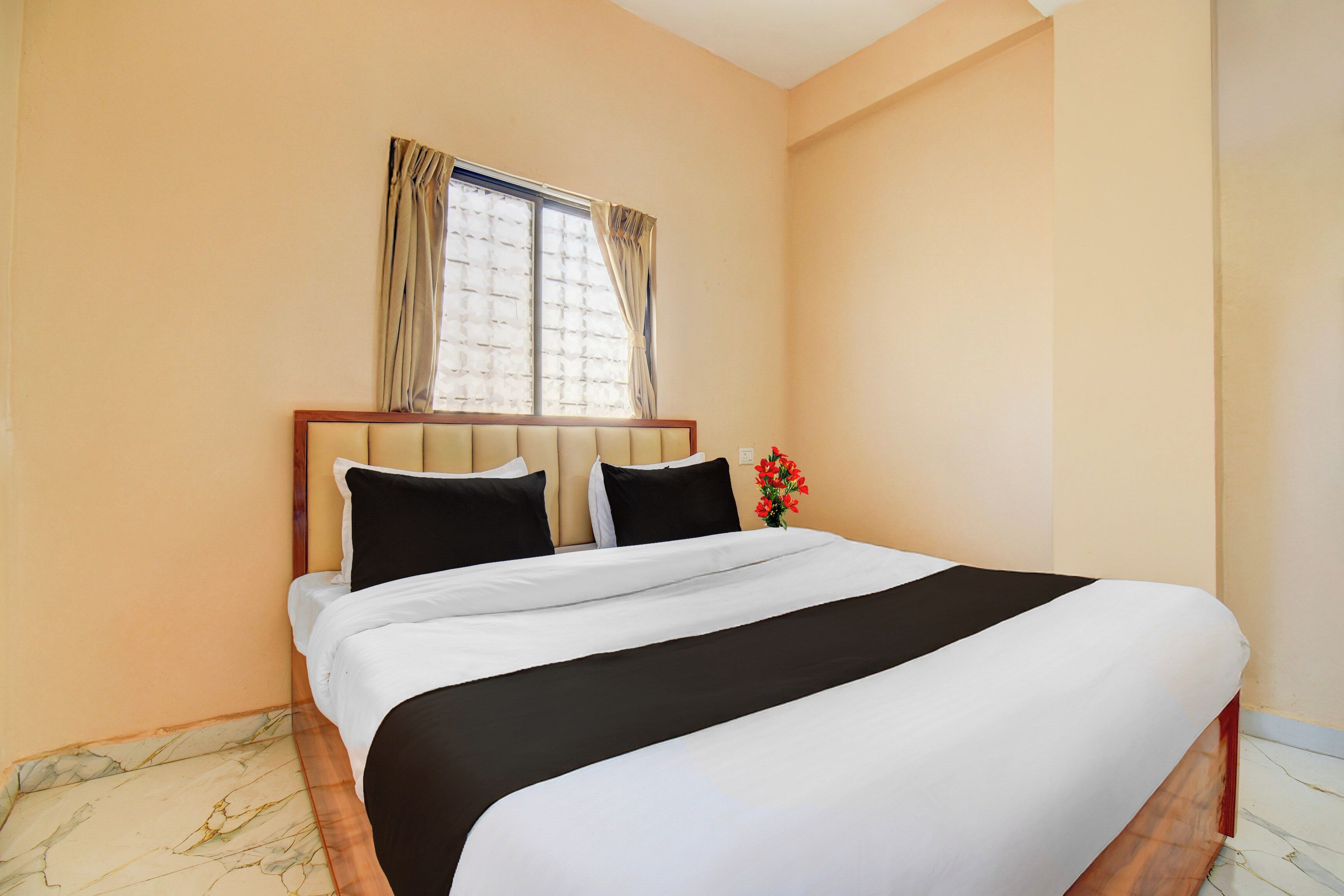 A hotel room with a large bed, a window with curtains, and a vase with flowers.
