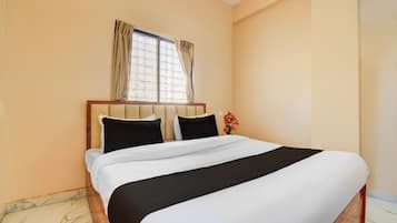 A hotel room with a large bed, a window with curtains, and a vase with flowers.