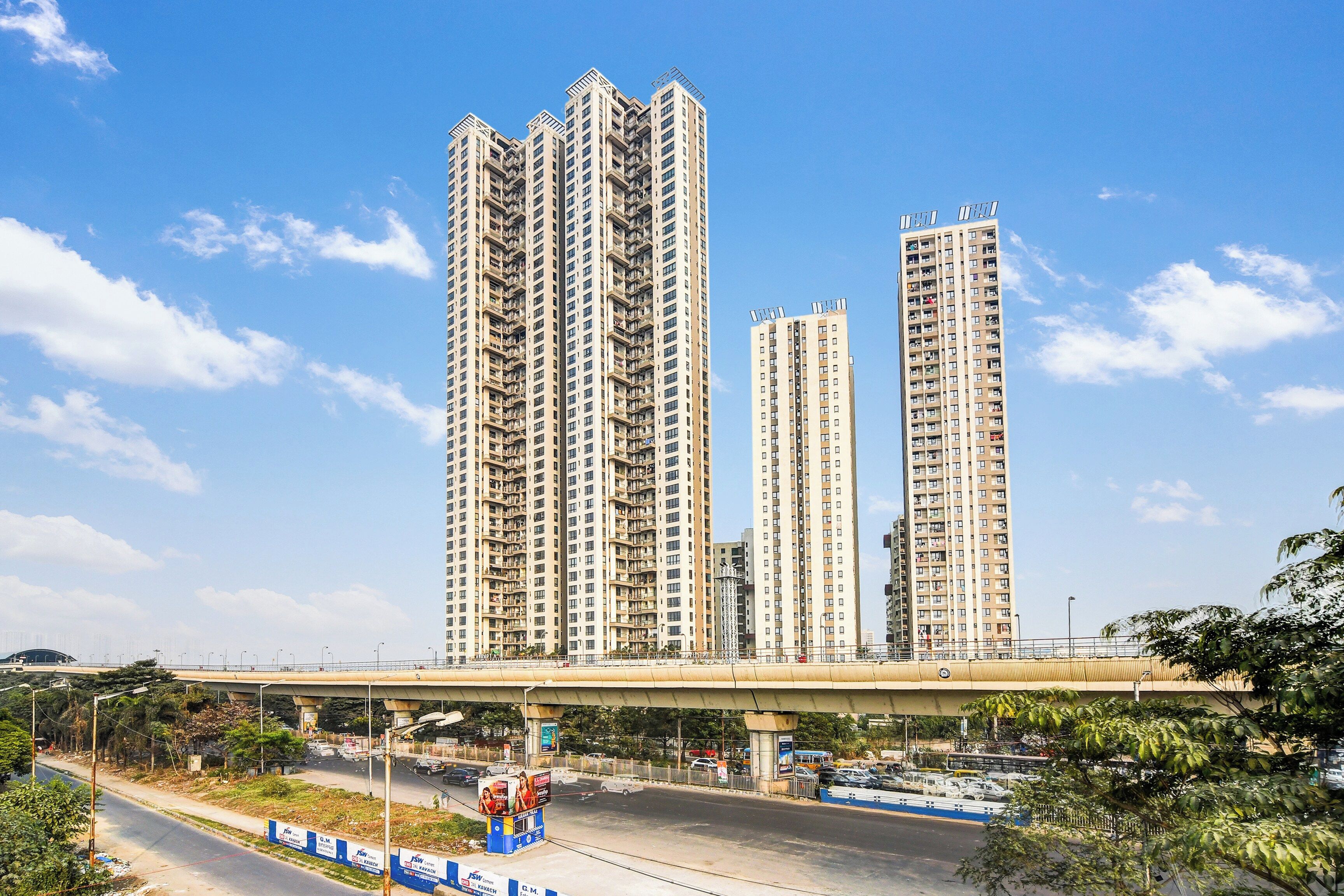 Un ensemble immobilier résidentiel composé d’immeubles à étages, avec plusieurs bâtiments d’appartements, un pont enjambant l’ensemble et une route où circulent des véhicules, dont un autobus.