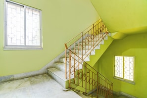 Una escalera con barandilla de metal que lleva a un rellano, una ventana con reja de metal y una pared verde.