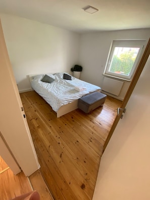 Ein kleines Zimmer mit einem Einzelbett, Holzboden, einem Fenster und einer Heizung.
