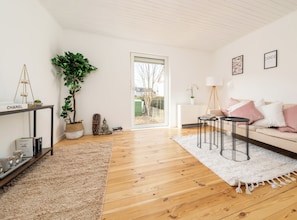 Ein modernes Wohnzimmer mit Holzboden, einem weißen Sofa, einem Couchtisch, einem Beistelltisch, einer Topfpflanze und einem Bücherregal.