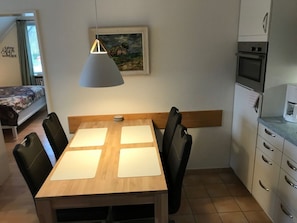 A compact room with a dining table, chairs, a painting, a bed, and a kitchenette. - 10 in Goting Huus (Wyk auf Foehr)