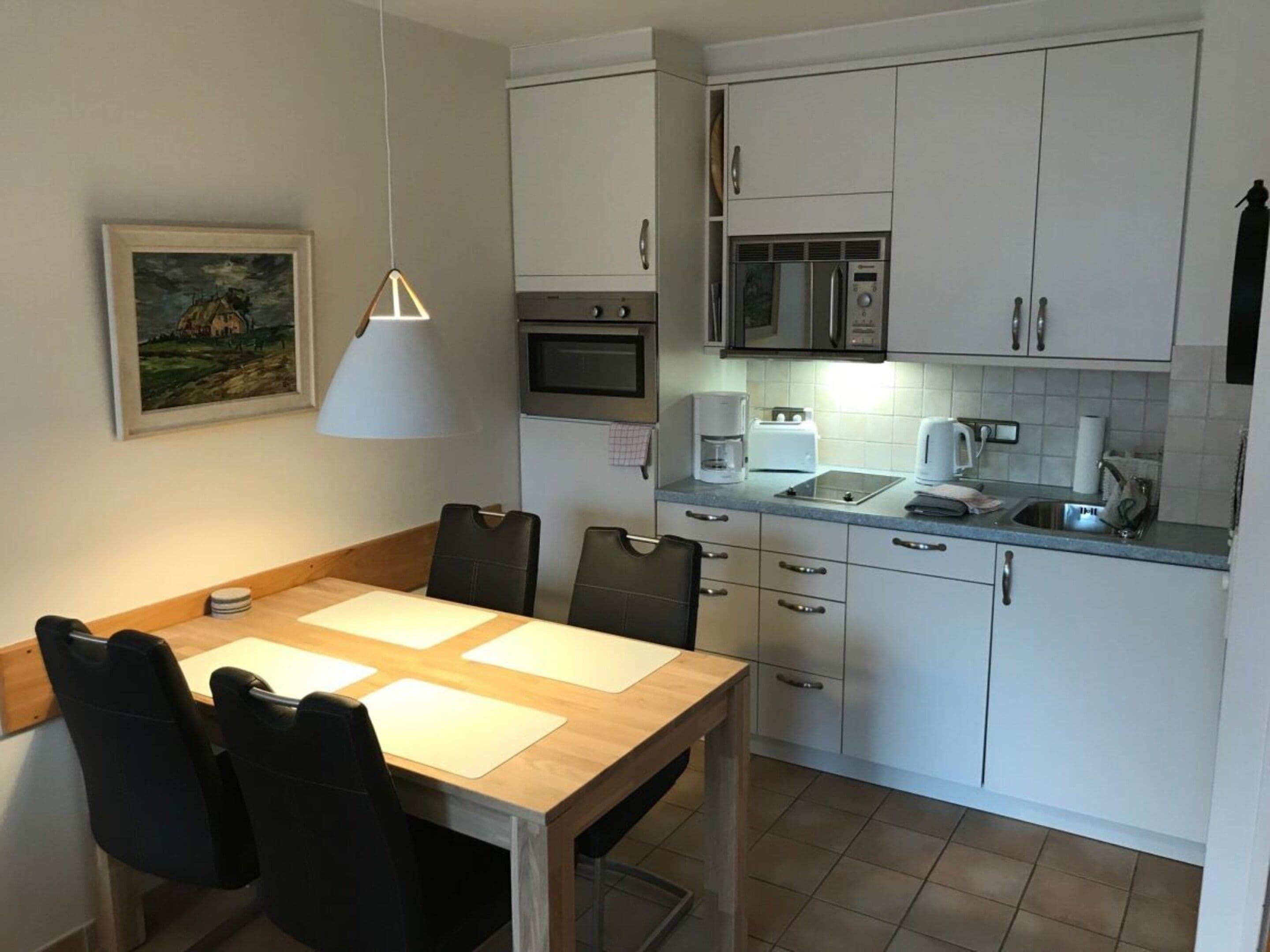 Een kleine keuken met witte kastjes, een magnetron, een koffiezetapparaat en een spoelbak.