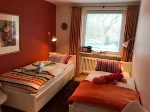 A small, cozy room with two beds, a radiator, a window with curtains, and a framed picture on the wall. - 10 in Goting Huus (Wyk auf Foehr)