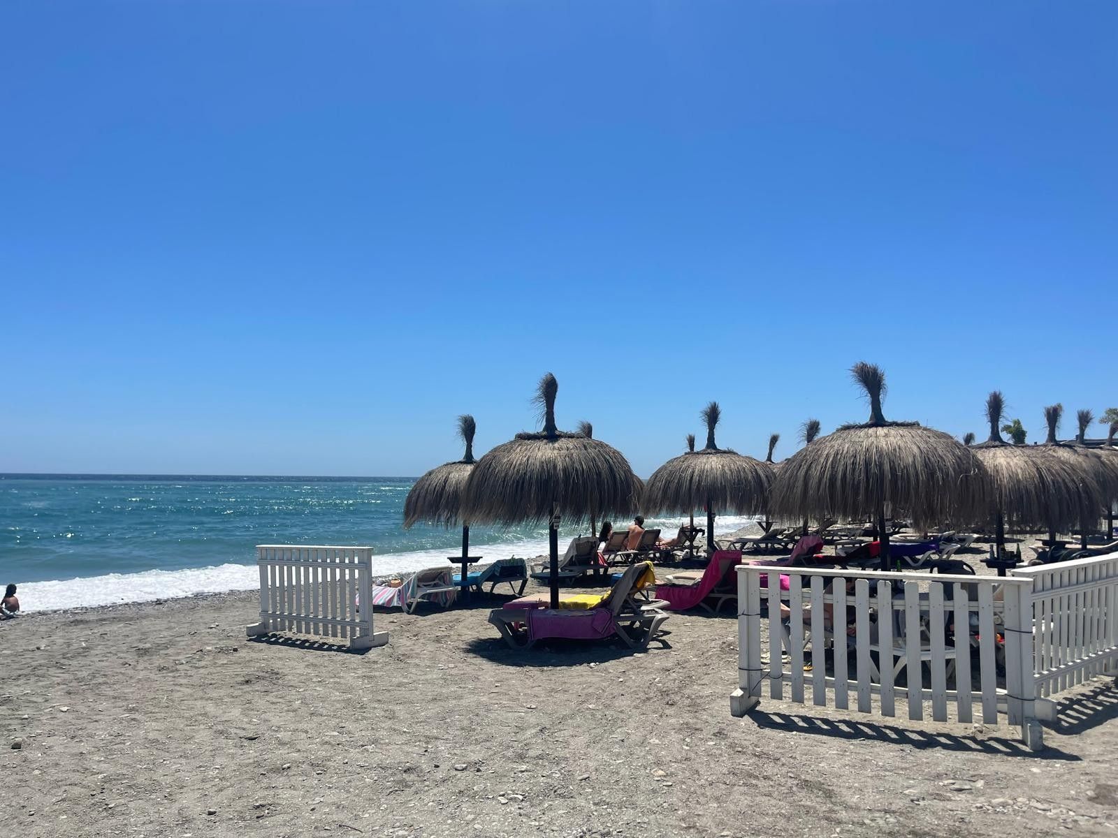 Una playa con sombrillas de paja y sillas de descanso.