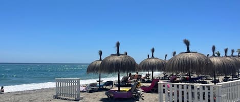 A beach with thatched umbrellas and lounge chairs.