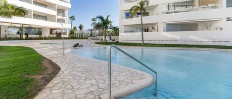 A modern hotel with a swimming pool, palm trees, and a clear sky.