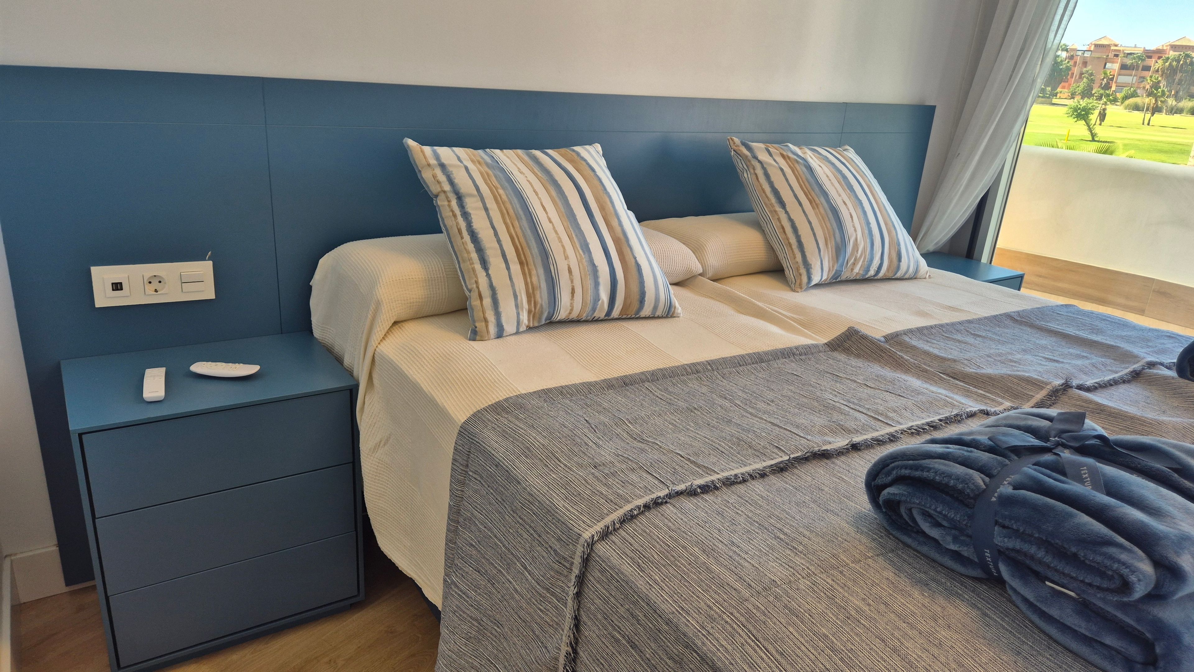 A hotel room with a bed, bedside tables, a remote control, and a view of the outdoors.