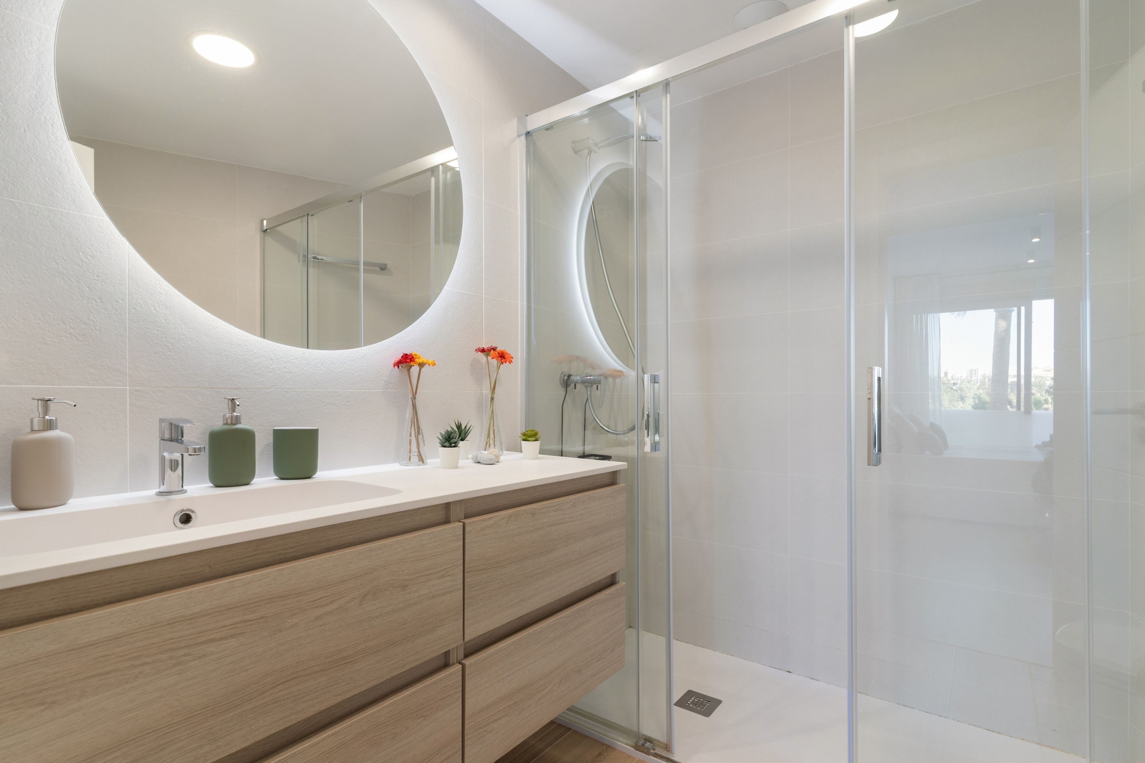 Een moderne badkamer met een grote spiegel, een douchecabine en een wastafelmeubel met een wastafel en opbergruimte.