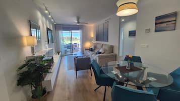 Una sala de estar moderna con una mesa de comedor de vidrio, sillas azules, un sofá y un ventilador de techo.