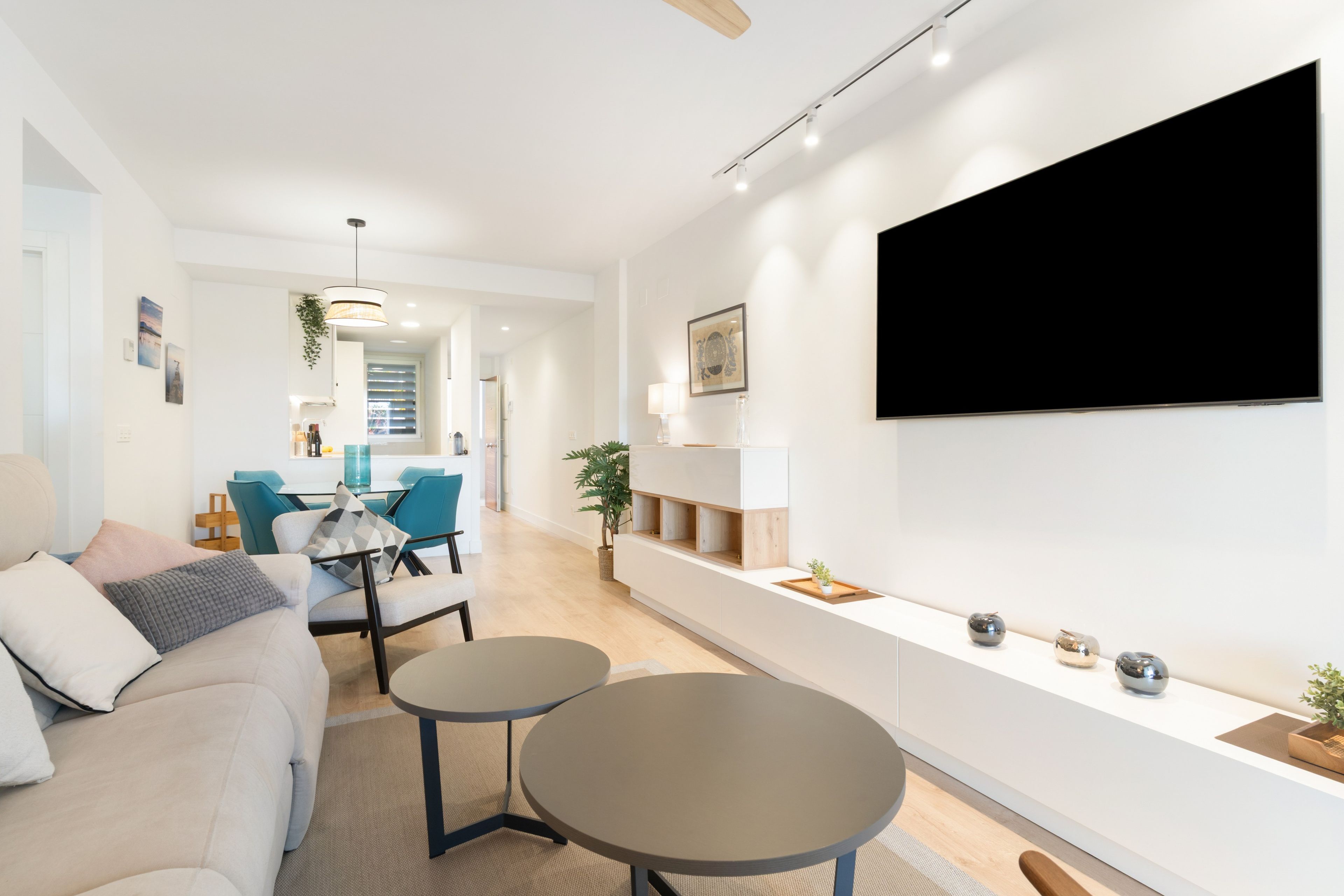 Un salon moderne avec un canapé, deux tables rondes, un téléviseur fixé au mur et une cuisine en arrière-plan.