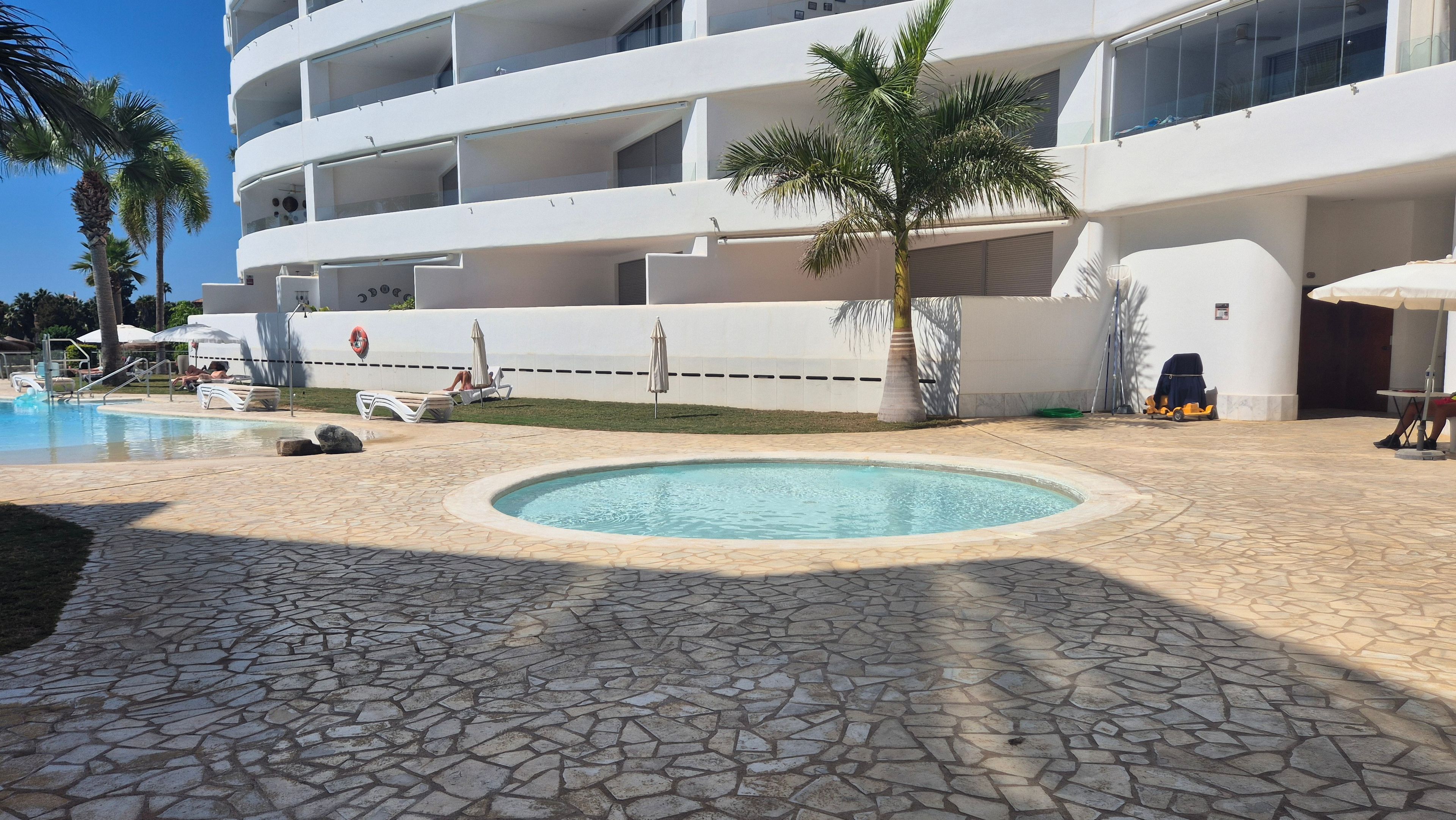 A pool area with a circular water feature, lounge chairs, and a building with multiple balconies.