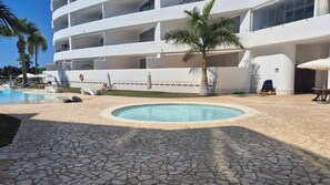 Un área de piscina con una fuente circular, sillones de descanso y un edificio con varios balcones.