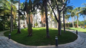 Un jardín ajardinado con palmeras, un camino pavimentado y un edificio de diseño moderno.