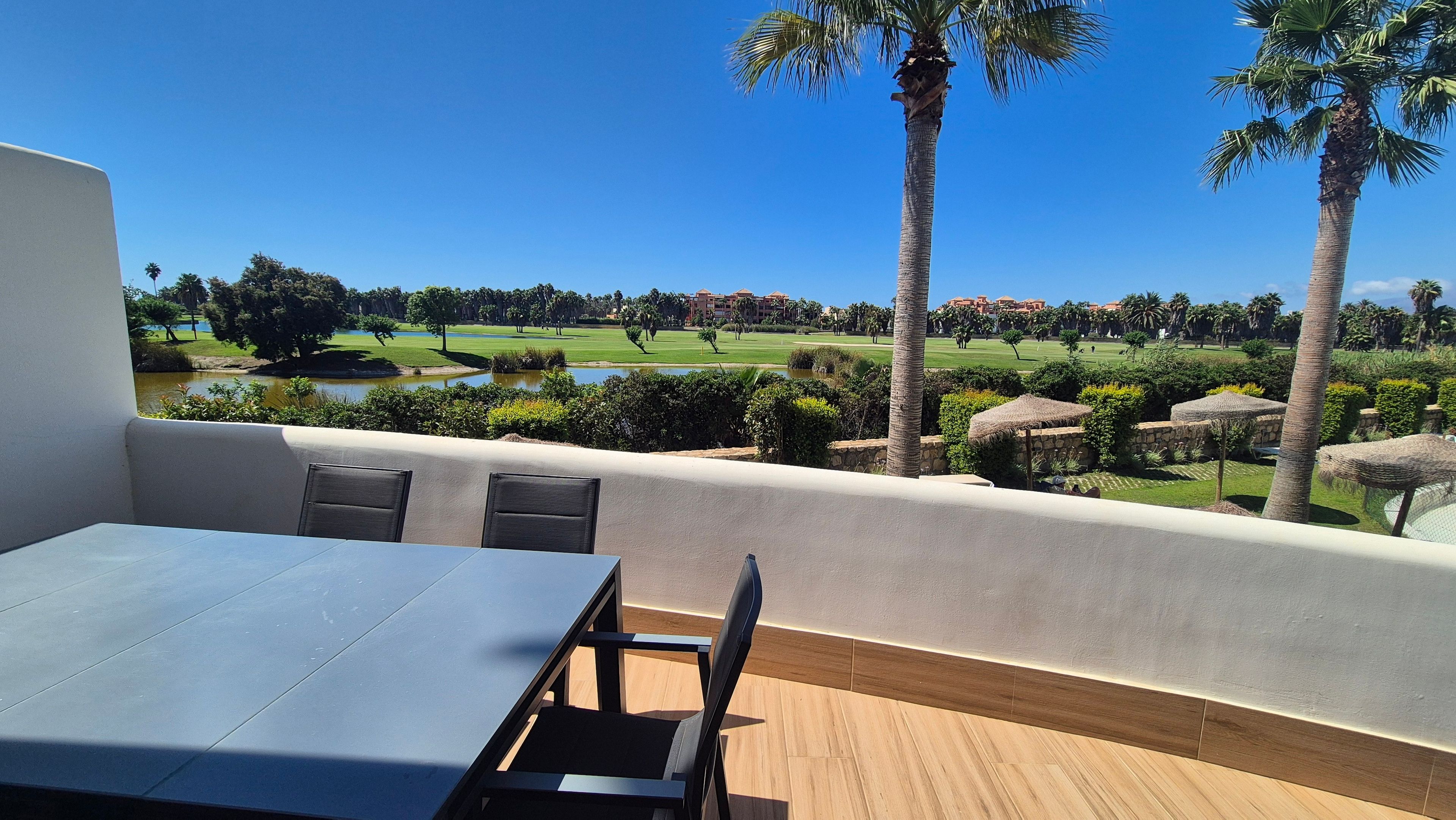 Una terraza con mesa y sillas, con vistas a un campo de golf y una masa de agua.