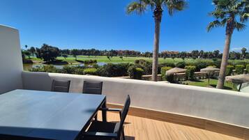 Una terraza con mesa y sillas, con vistas a un campo de golf y una masa de agua.