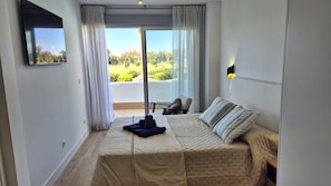 Une chambre à coucher avec un lit, une chaise, une télévision et un balcon avec des rideaux.