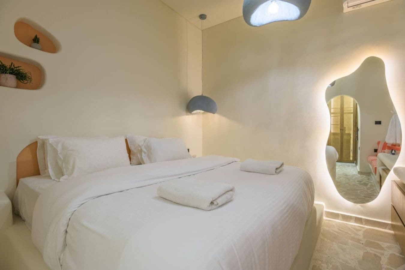 Un dormitorio con una cama grande, una lámpara de pared y un espejo que refleja un vano de puerta.