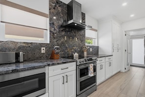 A modern kitchen with a built-in stove, oven, and microwave. There is a window with blinds, a countertop with a knife block, and a kettle. - The Cabana Club-3BR- Fantastic Outdoor Pool-Bar-TV (Fort Lauderdale)