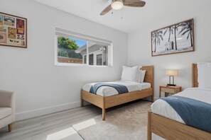 A bedroom with a bed, a nightstand, a chair, a ceiling fan, a window, and a wall with framed pictures. - The Cabana Club-3BR- Fantastic Outdoor Pool-Bar-TV (Fort Lauderdale)
