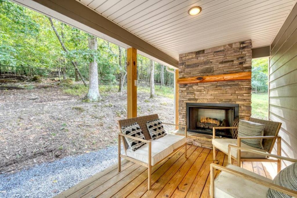 Une terrasse en bois avec une cheminée en pierre, deux fauteuils confortables et une vue sur une zone boisée.