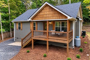 Een houten huis met twee verdiepingen, een balkon, een overdekte veranda en een kleine tuin.