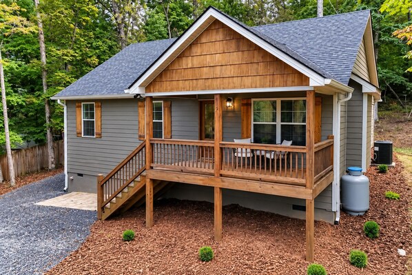 Une maison en bois à deux étages, dotée d’un balcon, d’un porche couvert et d’un petit jardin.