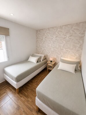 A bedroom with two beds, wooden flooring, a geometric-patterned wall, and a bedside table with a lamp. - New Listing (Íllora)