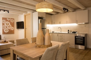 A modern kitchen with white cabinets, a stainless steel oven, and a dining area with a wooden table and chairs. - Alto Loft by CorfuEscapes (Corfu)