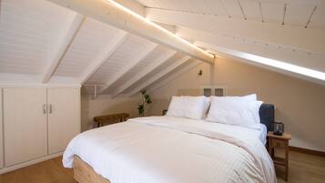 A bedroom with a sloped ceiling, a bed with white bedding, a bedside table with a lamp, and a small plant.