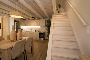 A modern kitchen with white cabinets, a dining area with a wooden table and chairs, and a staircase leading to an upper level. - Alto Loft by CorfuEscapes (Corfu)