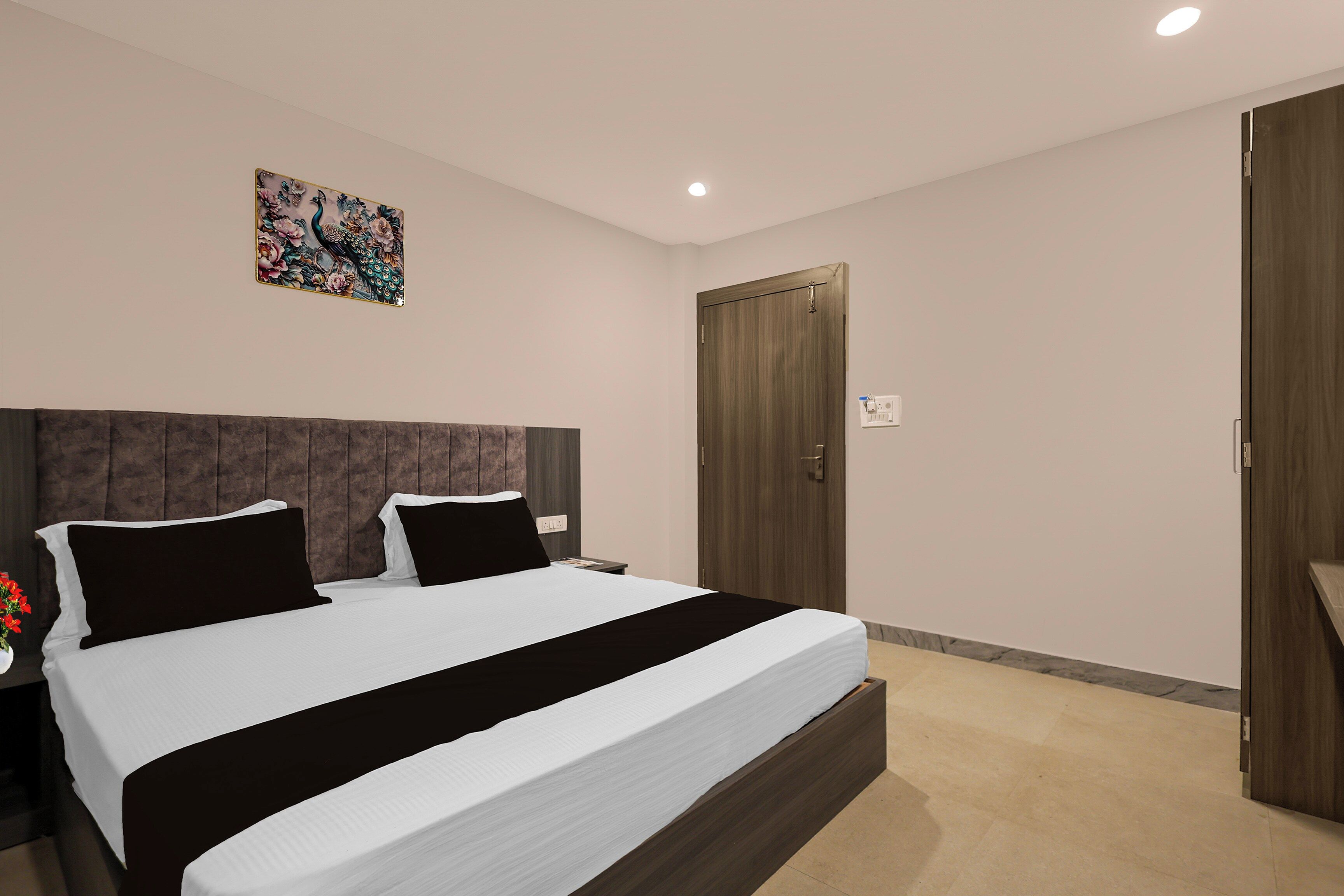 Un dormitorio con una cama grande, cabecera, mesita de noche, luz de pared y una puerta.