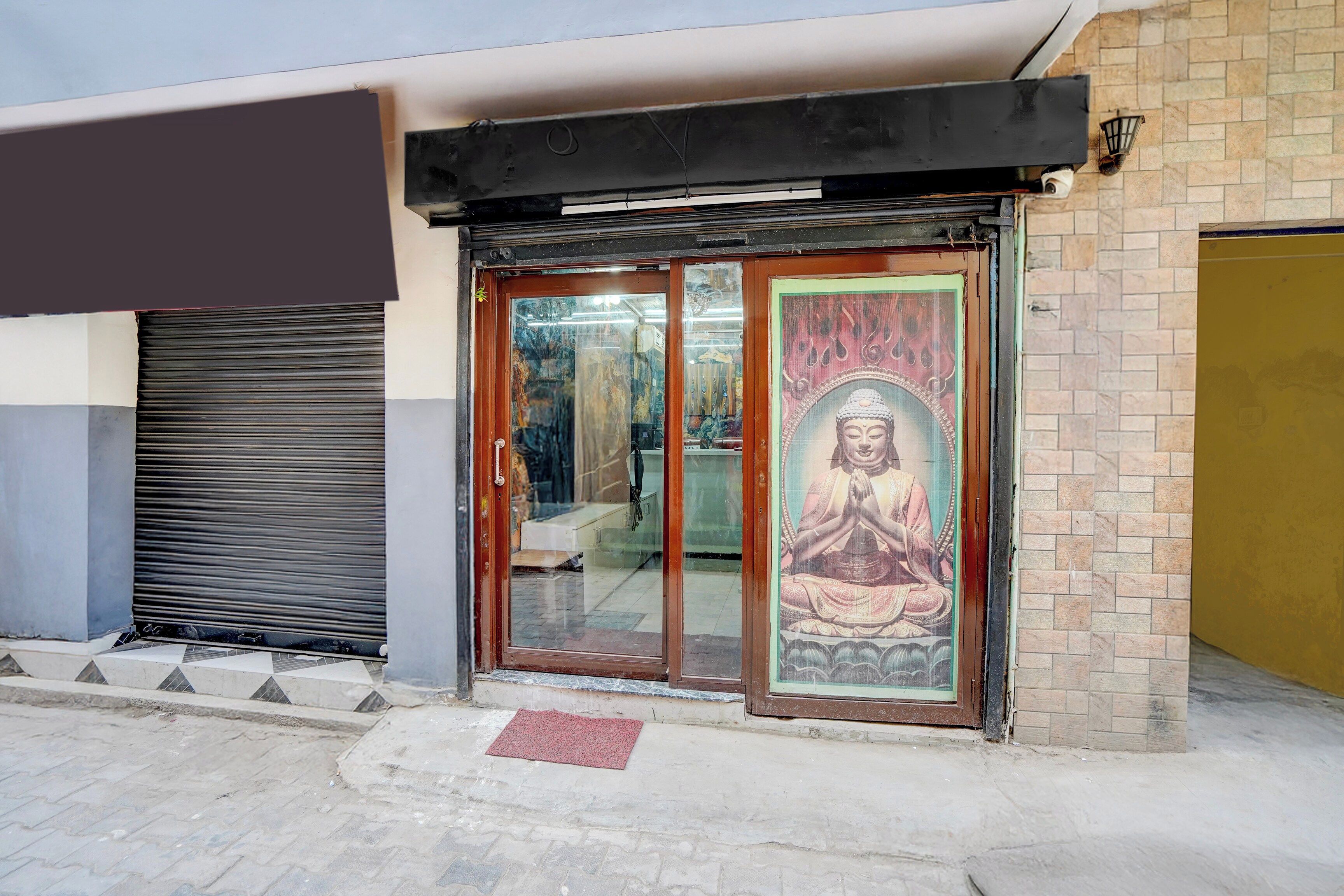 A building entrance with a glass door, a mural of a seated figure, and a closed shutter to the left.
