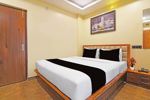 A hotel room with a large bed, a wooden headboard, a nightstand with a phone, a wall-mounted light, and a painting of a building.