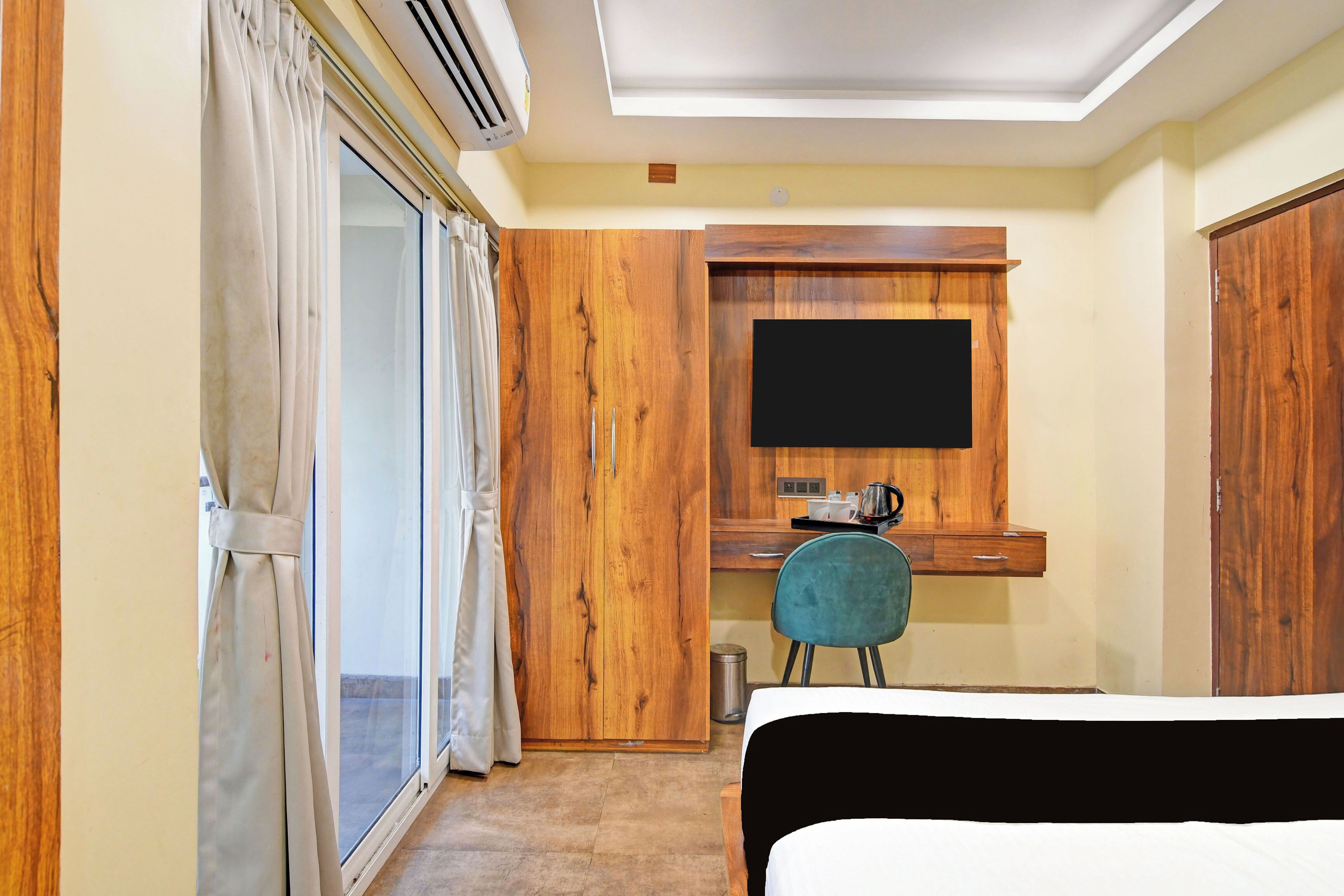 A hotel room with a bed, a desk with a chair, a television mounted on the wall, and a sliding glass door.
