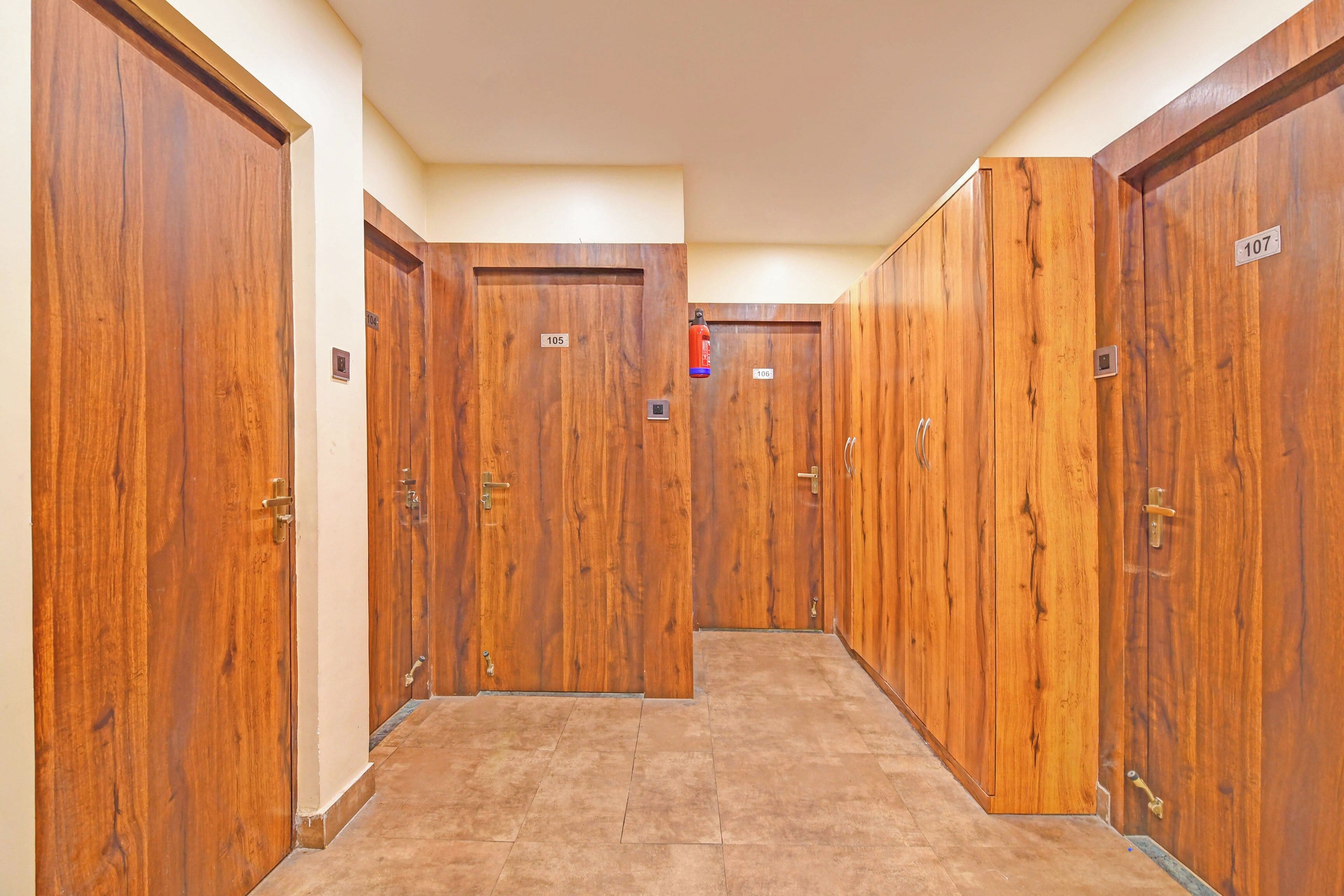 A hallway with wooden doors numbered 104 to 107, each with a doorbell and a fire extinguisher mounted on the wall.