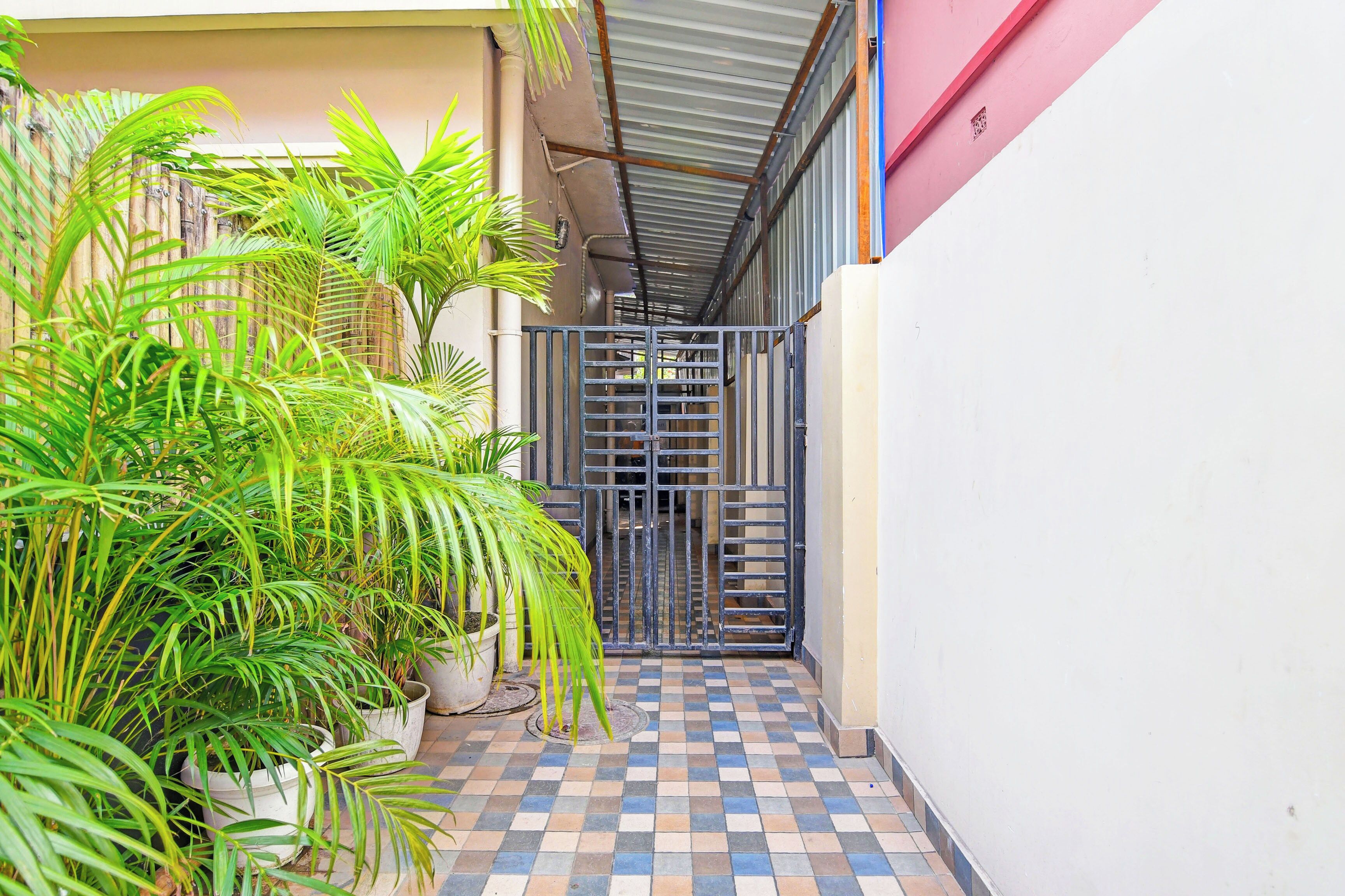 A narrow corridor with a tiled floor, a metal gate, and potted plants.