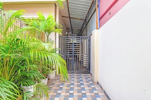 A narrow corridor with a tiled floor, a metal gate, and potted plants.